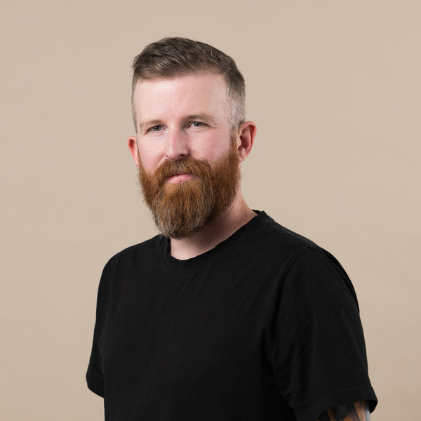 Person with a beard wearing a black shirt against a beige background