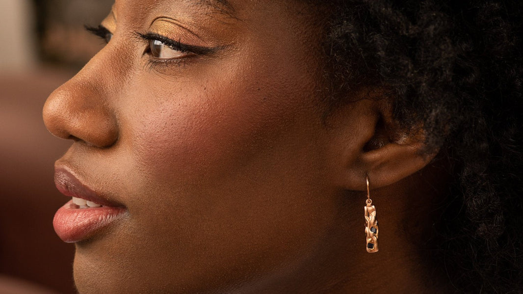 A femme presenting person's side profile, showing off their Malleable Kimberlite gold pendant earrings