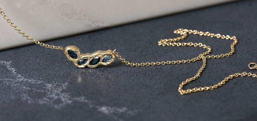 One of Malleable's gold chain necklaces draped on a tabletop. The pendant is made of 4 gems set in Malleable's signature Kimberlite style. 