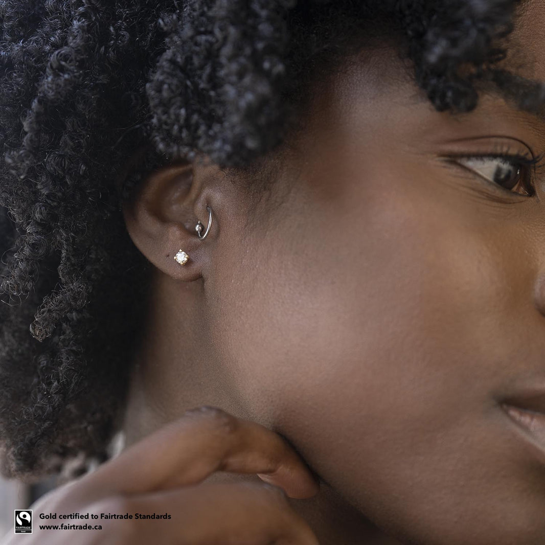 A partial portrait of a femme-presenting person facing right, showing off her diamond stud earrings from Malleable