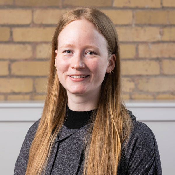 Person with long blonde hair smiling in front of a brick wall