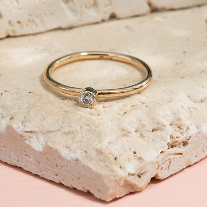 A high polish half round gold ring with a small bezel set diamond.