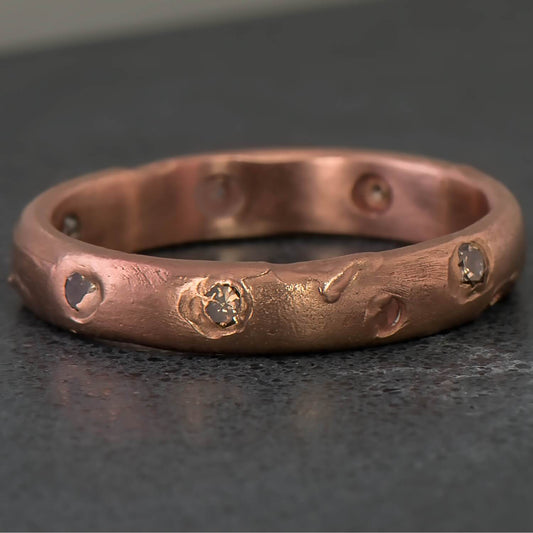 Recycled 14 karat rose gold set in cast ring containing 7 natural champagne round diamonds with a total weight of 0.58 carats. The band is 4mm in width and has a rough luxe textured surface with a half round profile.