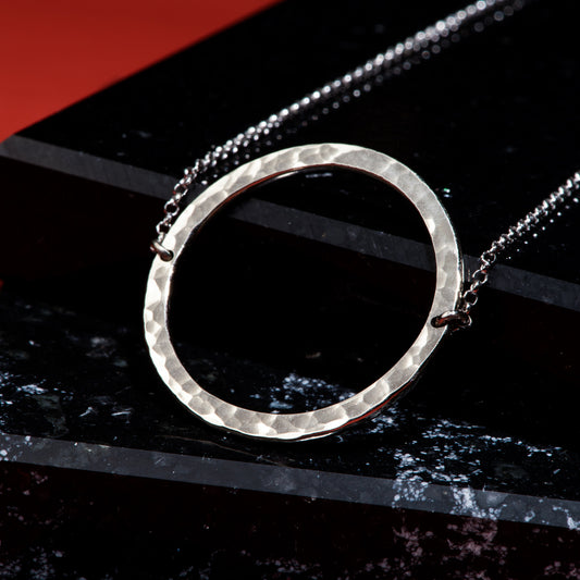 2.5 centimetre wide circular recycled white gold pendant with a hammer finish, attached to a 19" rolo chain.
