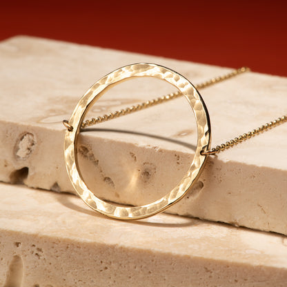 2.5 centimetre wide circular 10 karat recycled yellow gold pendant with a hammer finish, attached to a 19" rolo chain.