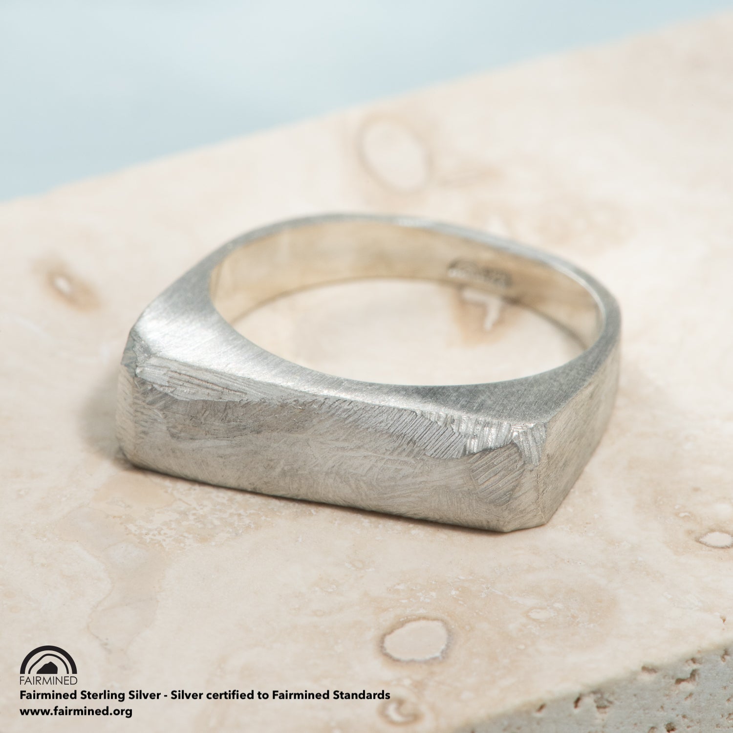 A carved, squared top silver signet ring with a brushed finish.