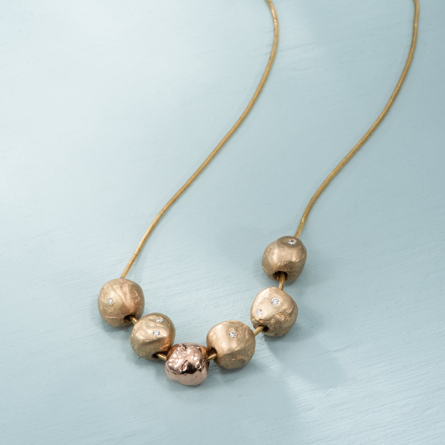 Rounded pebble shaped nuggets of brushed and polished yellow and rose gold, with flush set diamonds, on a yellow gold snake chain.