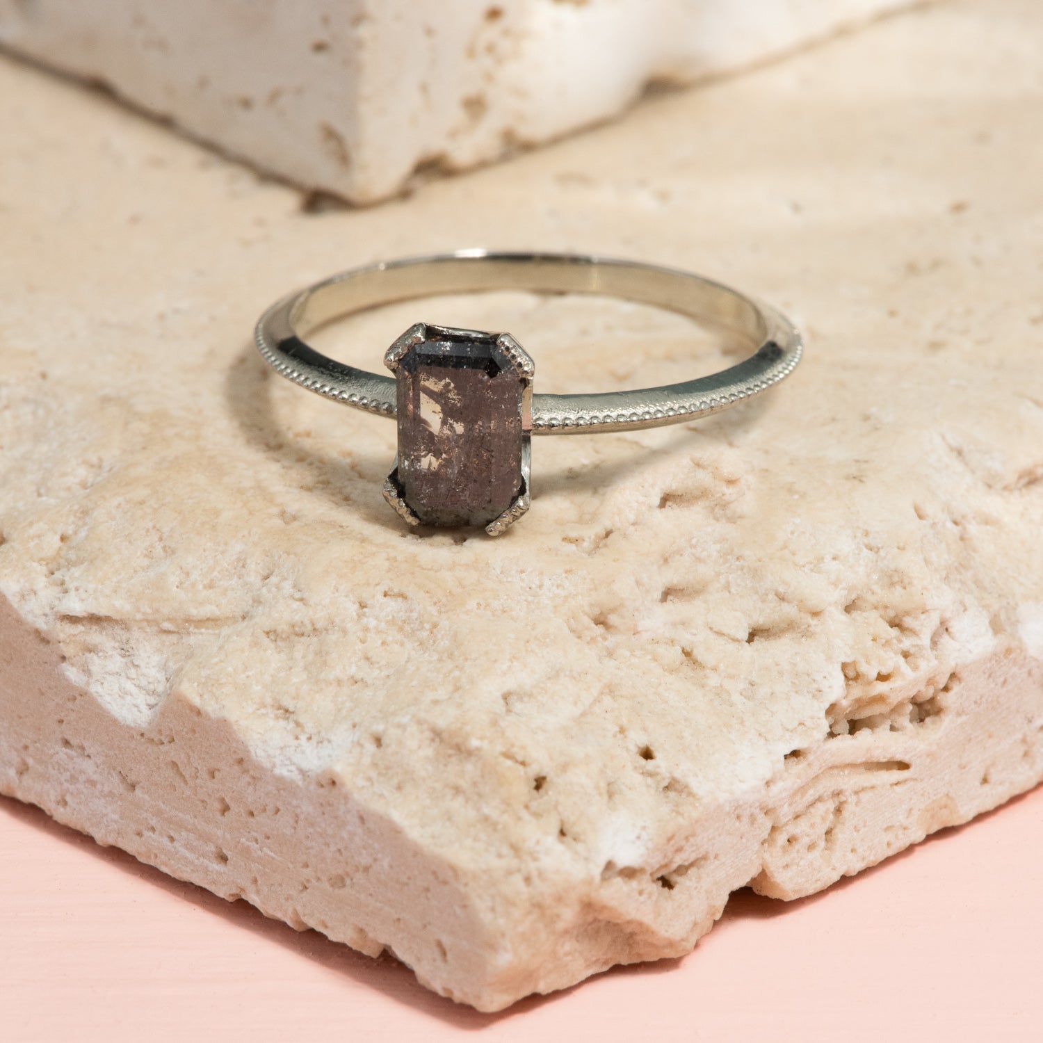 Milgrain prongs hold an emerald cut salt and pepper diamond on a milgrain band.