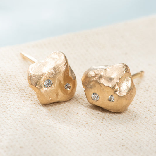 Pebble shaped yellow gold nuggets on stud earrings. Satin finished, with 2 flush set diamonds each.