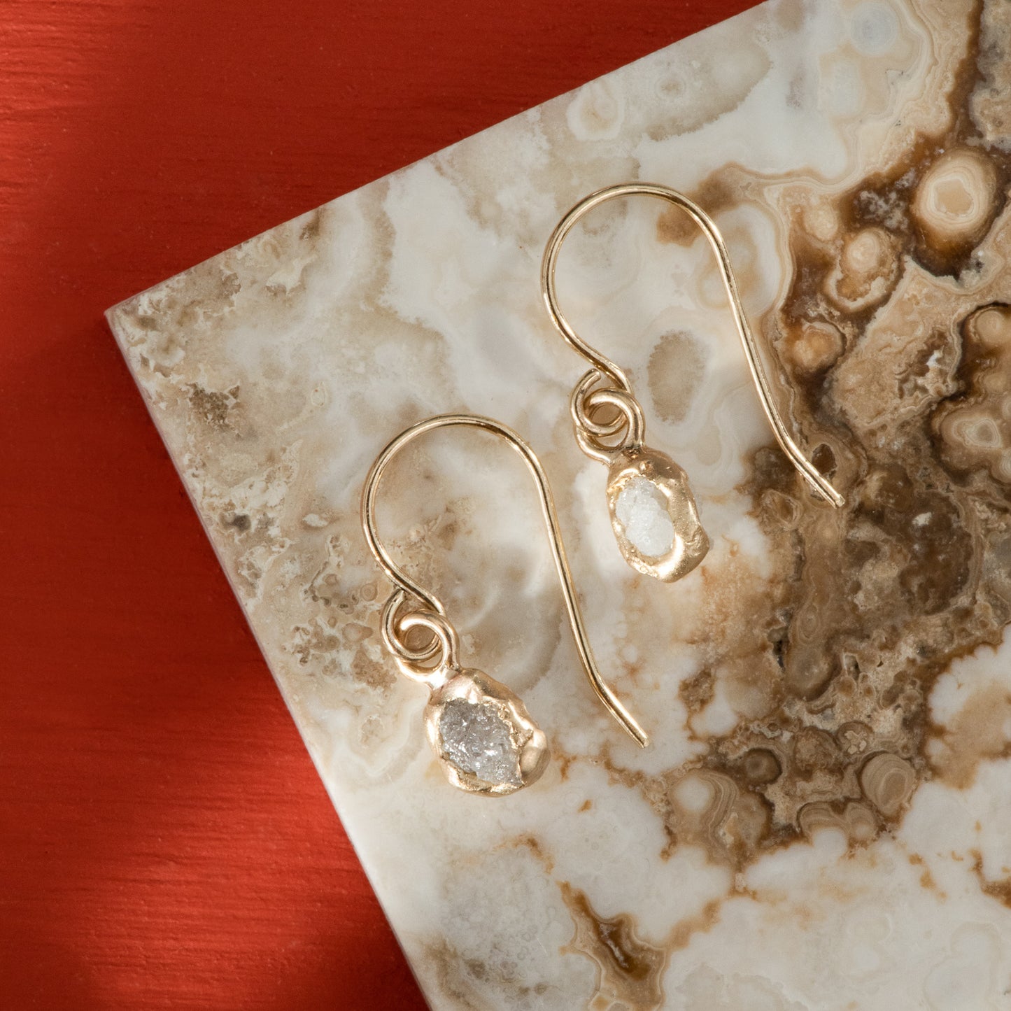 Polished yellow gold hook earrings, with a dangle of rough, grey diamond dipped in gold.