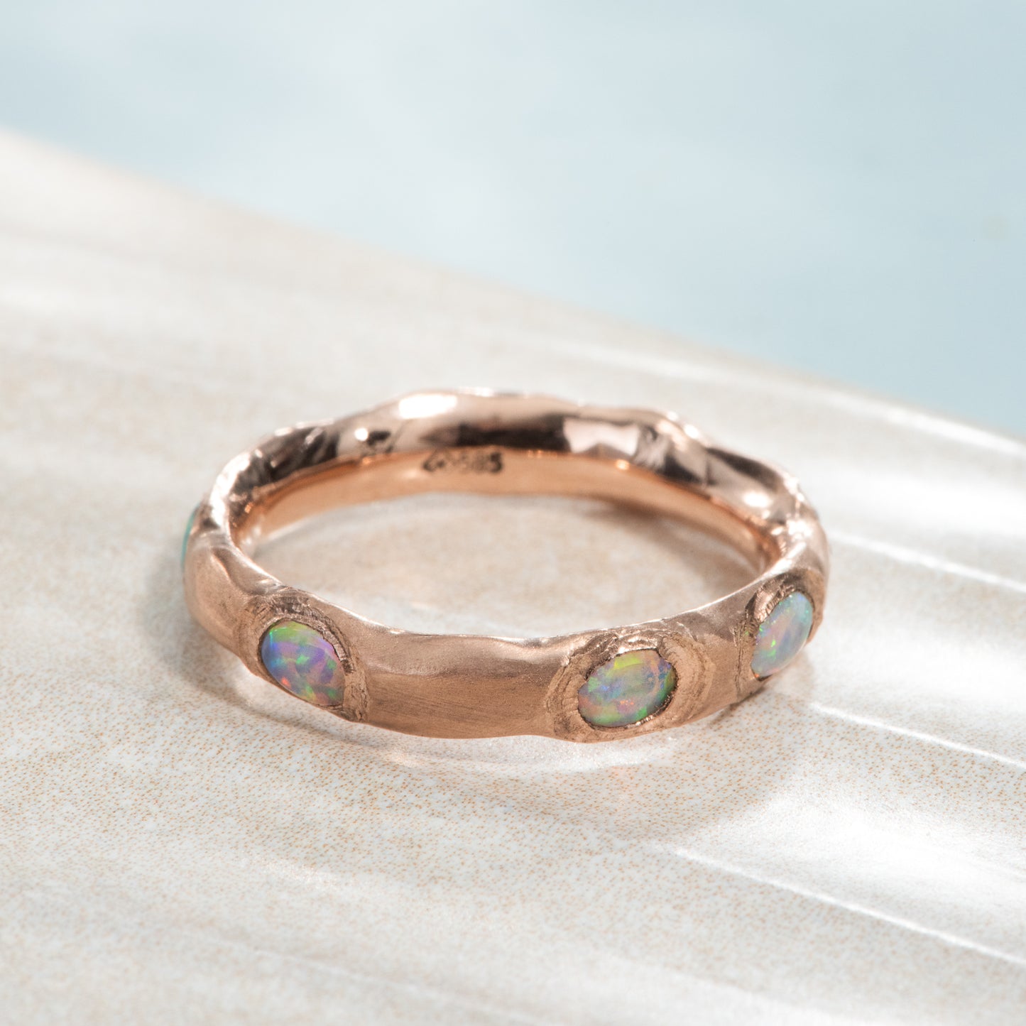 5 oval opals organically flush set all the way around a satin finished rose gold ring.