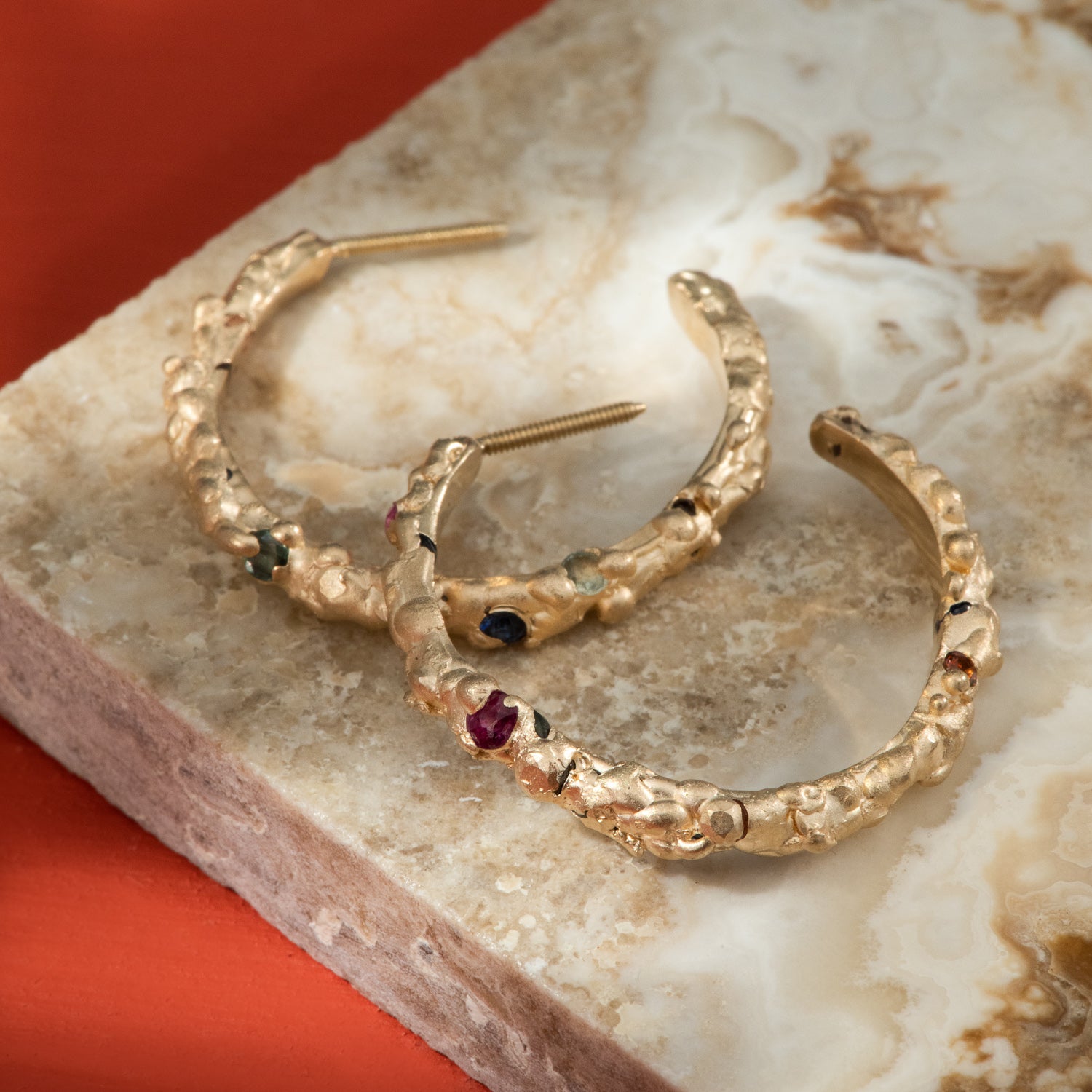 Many shades of sapphires organically flush set in satin finished gold hoops, with a bubbling texture.
