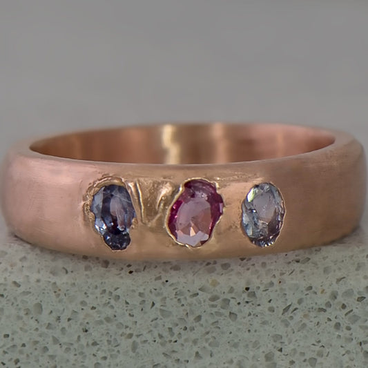 Recycled 14 karat rose gold Kimberlite ring with three oval sapphires (2 violet & 1 pink) in which have a total wight of 0.58 carats in which have been set in cast. The ring has a tapered half round profile in which ranges from 5mm at the top to 3mm at the bottom of the ring.
