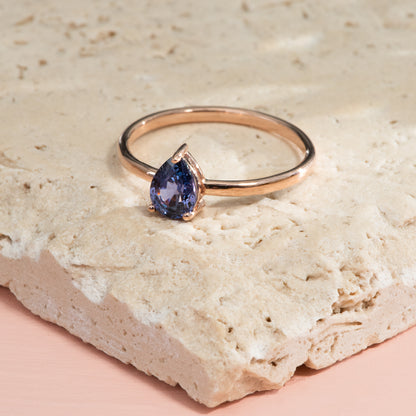 A pear cut purple-blue sapphire solitaire, on a thin rose gold band.
