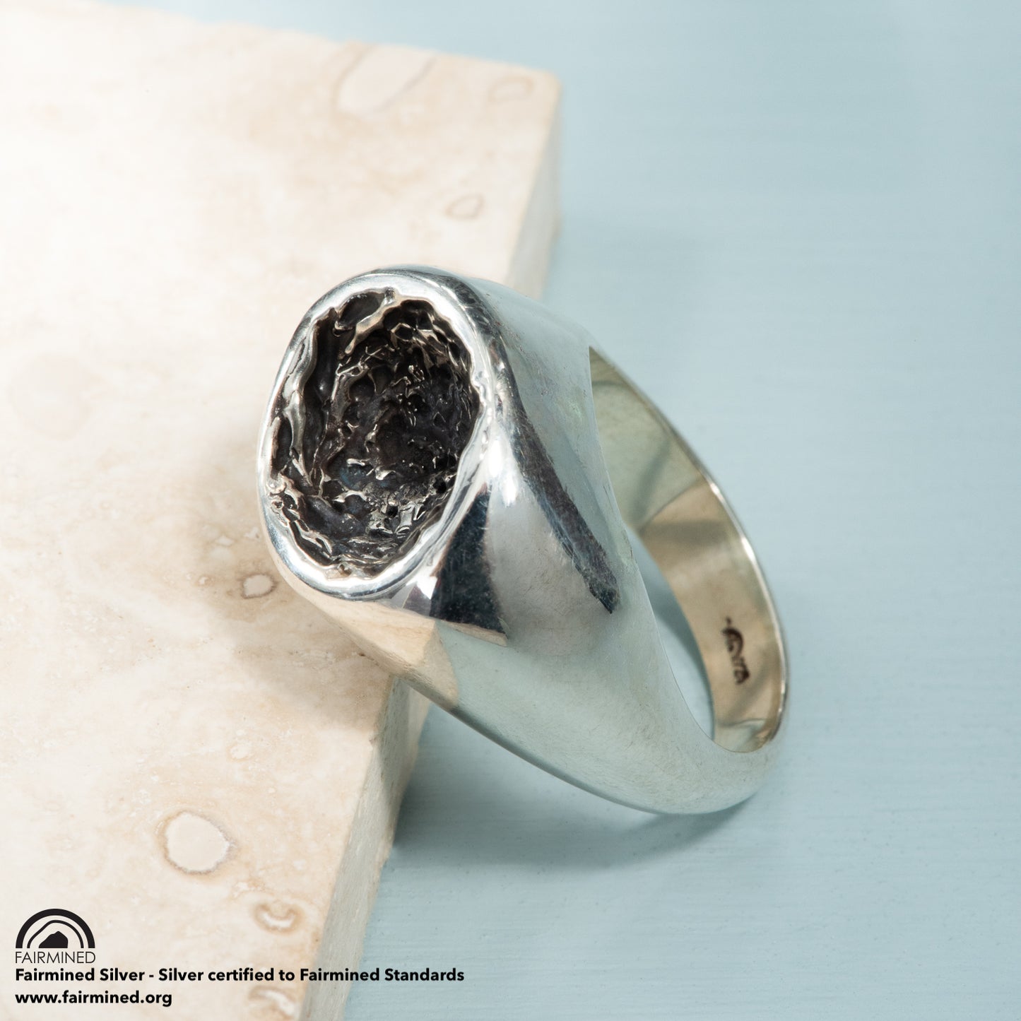 A concave, oxidized and pitted cup in a polished silver band.