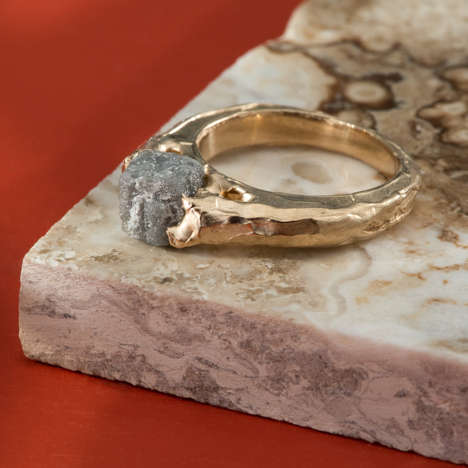 A rough, grey diamond set into a rustic and polished yellow gold band