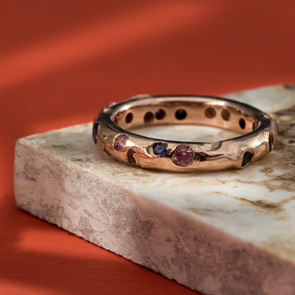 Multiple pink & purple sapphires, flush set all the way around a rose gold band.