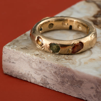 Multiple green, yellow, and orange sapphires set all the way around a burnished yellow gold band.