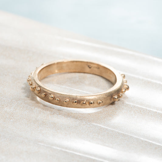 A satin finished yellow gold band, with tiny polished yellow gold beads all the way around the ring.