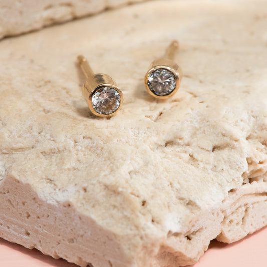 Round diamond stud earrings, bezel set in yellow gold.