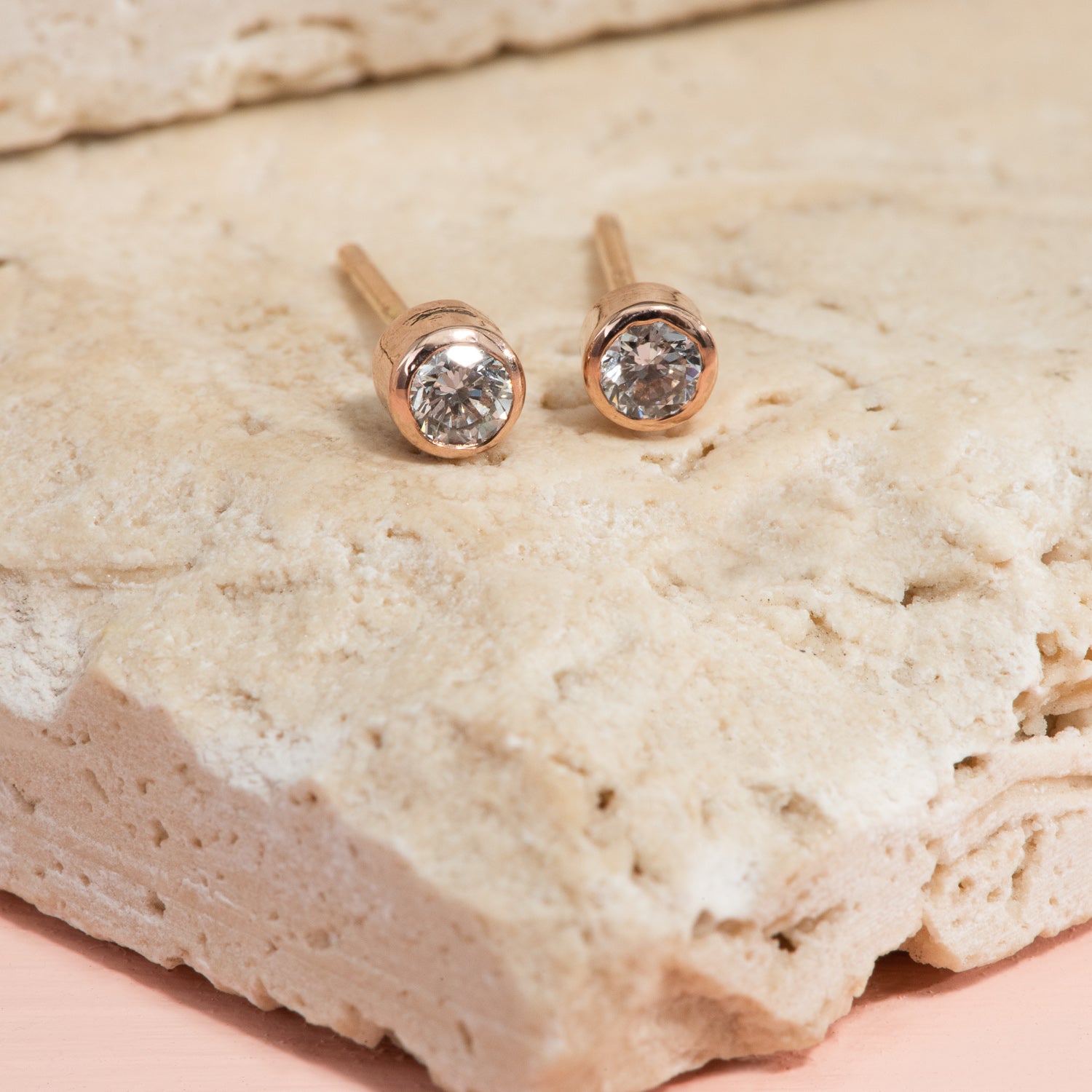 Round diamond stud earrings, bezel set in rose gold.