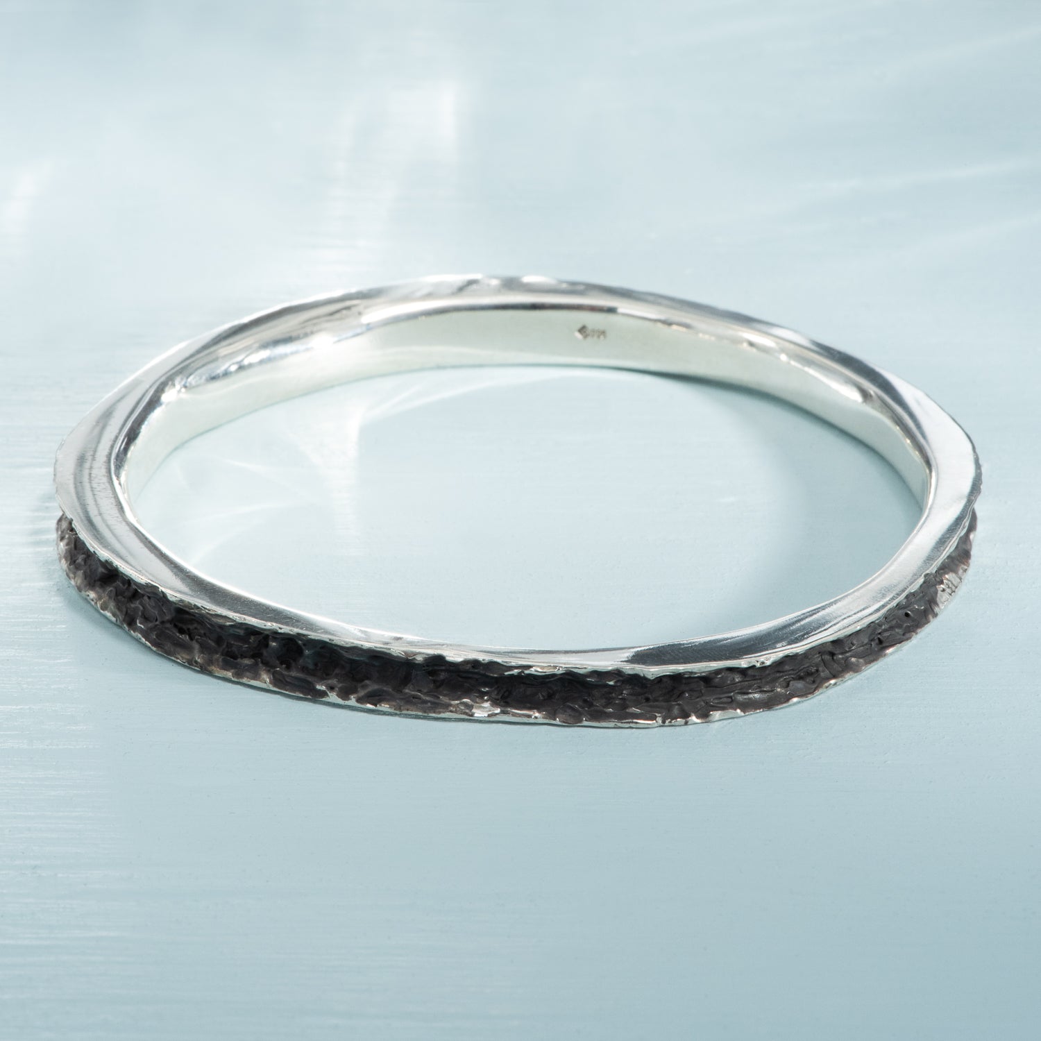 A textured, oxidized silver bangle bracelet, with a thin rim of polished silver.
