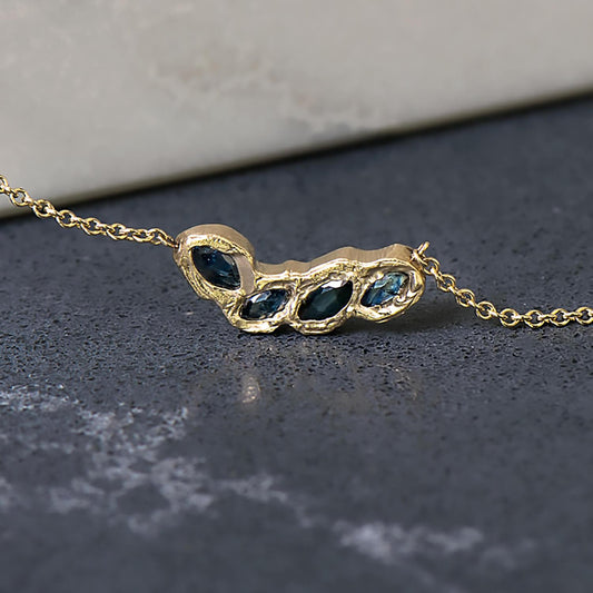 Recycled 14 karat yellow gold set in cast necklace. The rolo necklace is 20" in total length with the centre piece being 20mm containing 4 4mm x 2mm natural blue recycled marquise cut sapphires in a flush set textured surface.