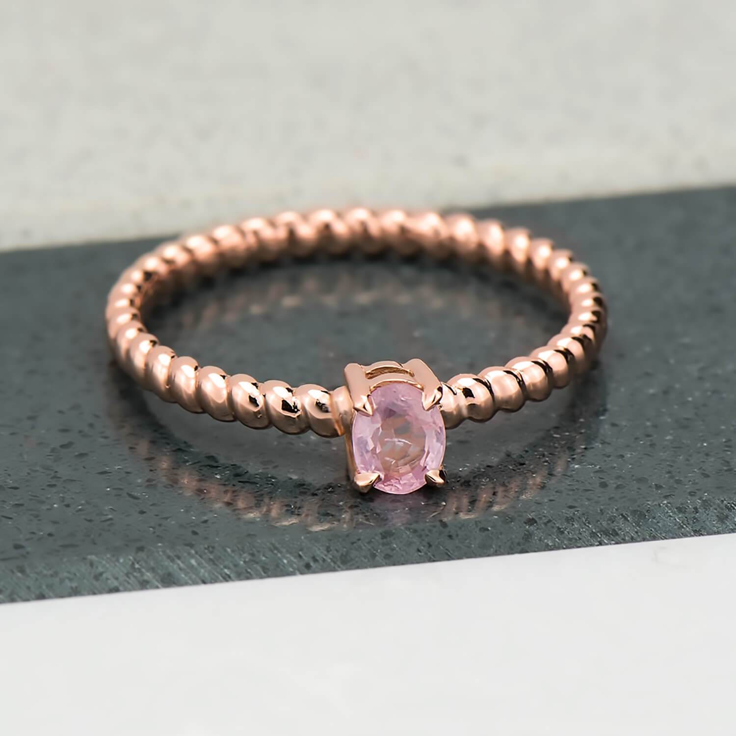 Recycled 14 karat rose gold spiral ring i which has been brought to a high polish. A four prong setting holds a natural 0.29 carat oval pink sapphire.