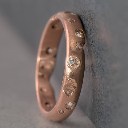14 karat recycled rose gold wedding ring with 13 natural colourless recycled round diamonds in which have been set in cast. The profile of the ring is half round and the surface is a rich texture with a medium sheen.